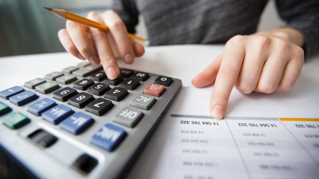 Person calculating costs with a calculator and document, estimating expenses to export car from Dubai.