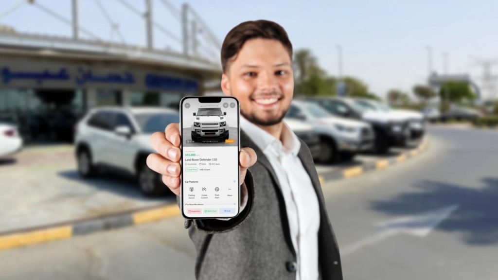 A man holding his phone while browsing cars available at Ras Al Khor car market.